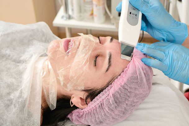 Mujer joven en el salón de belleza haciendo el procedimiento de pelado por ultrasonido y limpieza facial. - Foto, imagen