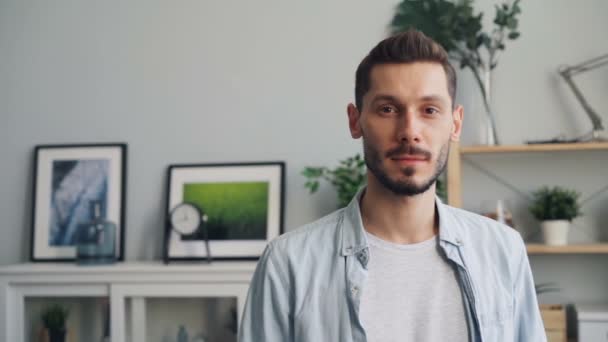 Slow motion portrait of handsome young man looking at camera standing at home - Imágenes, Vídeo