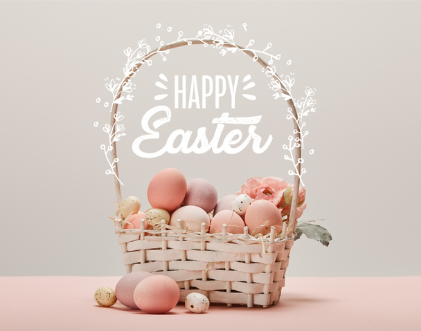 wicker basket with pink painted eggs, flowers and happy Easter lettering on grey background - Fotó, kép