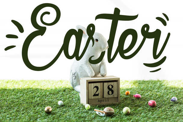 conejo decorativo, calendario de madera con fecha 28 de abril, y coloridos huevos de Pascua sobre hierba verde con letras de Pascua
 - Foto, imagen