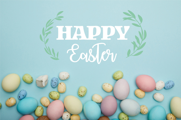 top view of painted multicolored eggs scattered and decorative bunny on blue background with happy Easter lettering - Photo, image