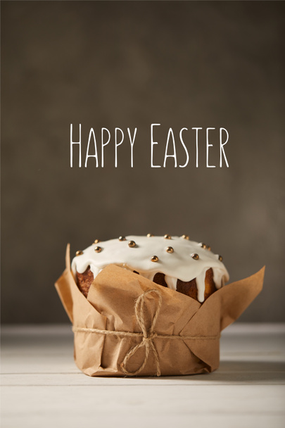 traditional decorated Easter cake in craft paper on white table with happy easter lettering on brown background - Foto, immagini