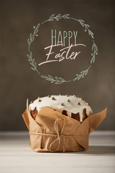 traditional decorated Easter cake in craft paper with happy easter lettering in circle on brown background - Foto, afbeelding