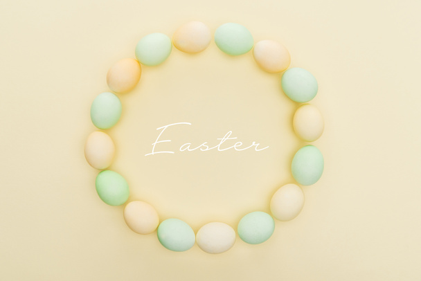pohled na zaoblený rám vyrobený z malovaných kuřecích vajíček na světle žlutém pozadí s Velikonocemi - Fotografie, Obrázek