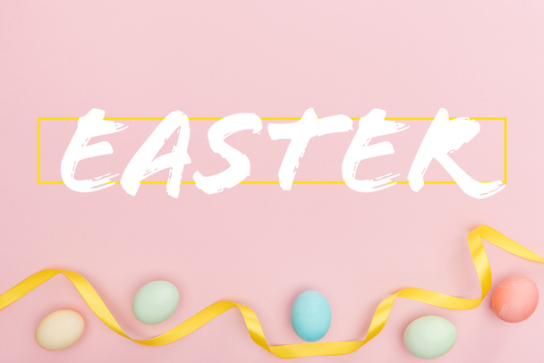 top view of painted multicolored chicken eggs and satin ribbon on pink background with Easter lettering - Foto, imagen