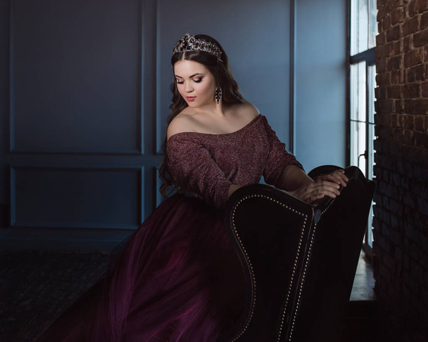 portrait of beautiful young pretty cute woman princess (queen) in long purple queen's dress and crown, with long hair and make up  indoor in minimalistic interior - Photo, Image