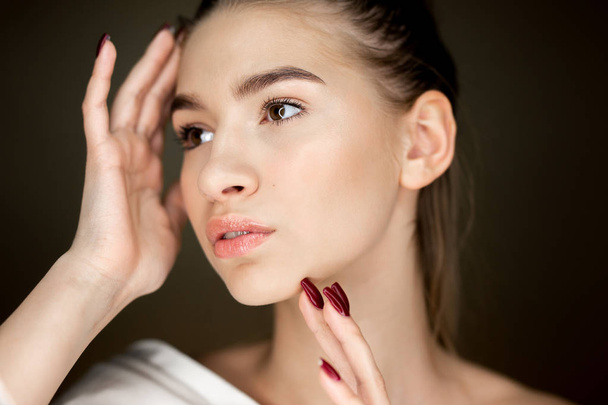 Portrait of young charming girl with natural makeup holding her hands on her face - Foto, Imagen