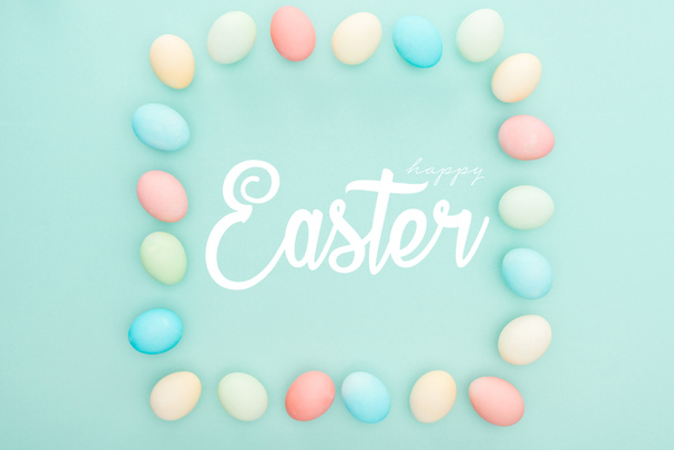 top view of square frame made of painted chicken eggs on blue background with white happy Easter lettering - Фото, изображение