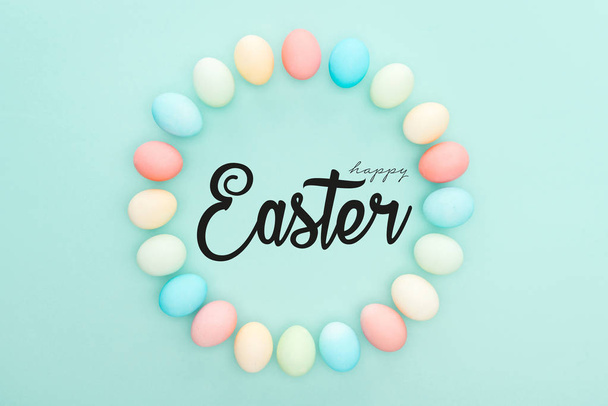 top view of round frame made of painted chicken eggs on blue background with black happy Easter lettering - Foto, Imagen