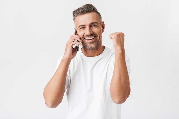 Image of happy man 30s wearing casual t-shirt holding smartphone - Фото, изображение