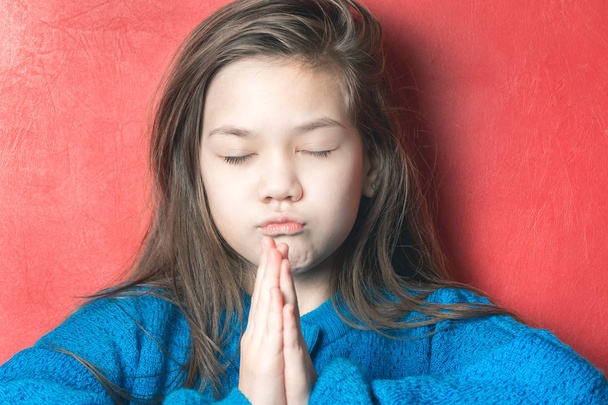 Красивая девушка в синем потрошителе молится на красном фоне
 - Фото, изображение