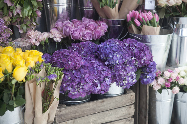 Pots with beautiful blooming pink and purple hydrangea flowers for sale outside flower shop. Garden store entrance decorated with rustic style wooden box and wicker flower pot. - Фото, зображення