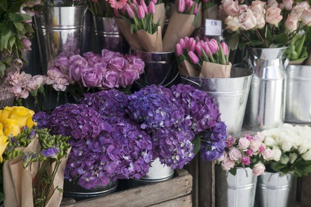 Pots with beautiful blooming pink and purple hydrangea flowers for sale outside flower shop. Garden store entrance decorated with rustic style wooden box and wicker flower pot. - Photo, image