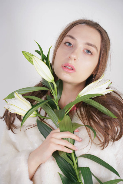 feminine girl in a white fur coat with a branch of lilies in the background in the Studio - Foto, immagini