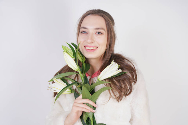 feminine girl in a white fur coat with a branch of lilies in the background in the Studio - 写真・画像