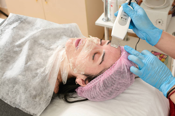 Mujer joven en el salón de belleza haciendo el procedimiento de pelado por ultrasonido y limpieza facial. - Foto, Imagen