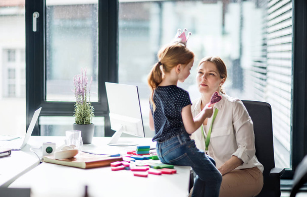 Een zakenvrouw met een kleine dochter zittend in een kantoor, werken. - Foto, afbeelding