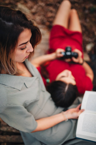 Mujeres jóvenes leyendo un libro y tomando fotos en el bosque
 - Foto, Imagen