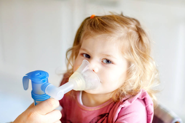 Little toddler girl making inhalation with nebulizer at home. Father or mother helping and holding the device. Child having flu, cough and bronchitis. asthma inhaler inhalation steam sick concept - Fotó, kép