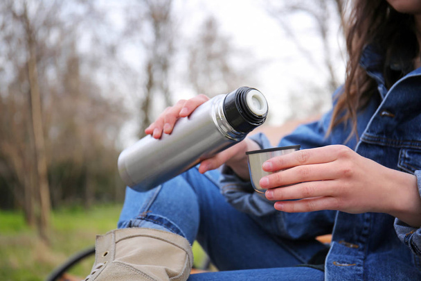 Woman drinking hot tea from thermos outdoors - Photo, Image