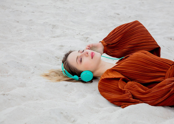 Jovem mulher na blusa cor Borgonha com fones de ouvido deitado
 - Foto, Imagem
