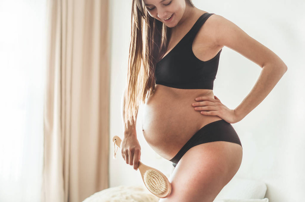 Gravidez e massagem seca. Mulher grávida segurando escova seca para cima de sua perna
 - Foto, Imagem