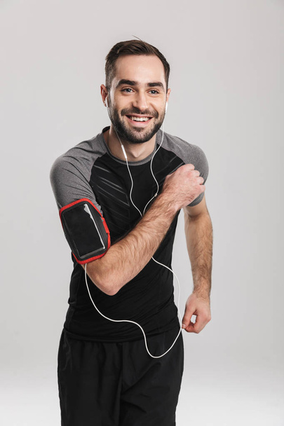 Handsome young sports fitness man posing isolate over white wall background listening music with earphones. - Photo, Image