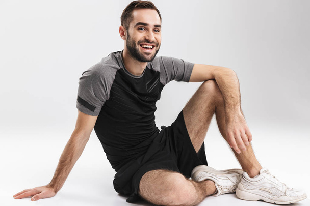 Young sports fitness man isolate over white wall background sitting on floor. - Φωτογραφία, εικόνα