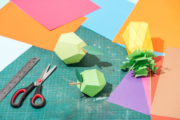 Origami-Früchte und bunte Pappe mit Schere und Lineal auf unordentlicher Oberfläche - Foto, Bild