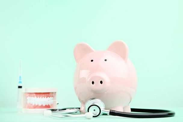 rosafarbenes Sparschwein mit Stethoskop und Zahnmodell auf Minzrücken - Foto, Bild