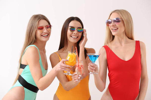 Krásné mladé ženy v plaveckých oblecích a koktejly na bílém pozadí - Fotografie, Obrázek