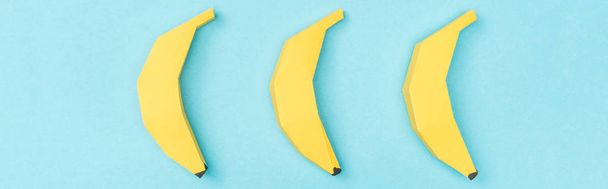 tiro panorâmico de bananas de papel amarelo dispostas Isolado em azul
 - Foto, Imagem