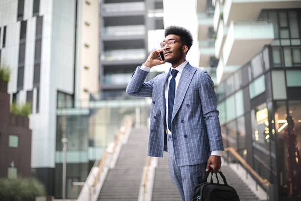 Elegant businessman walking in the street while taking at the phone - Foto, Imagen
