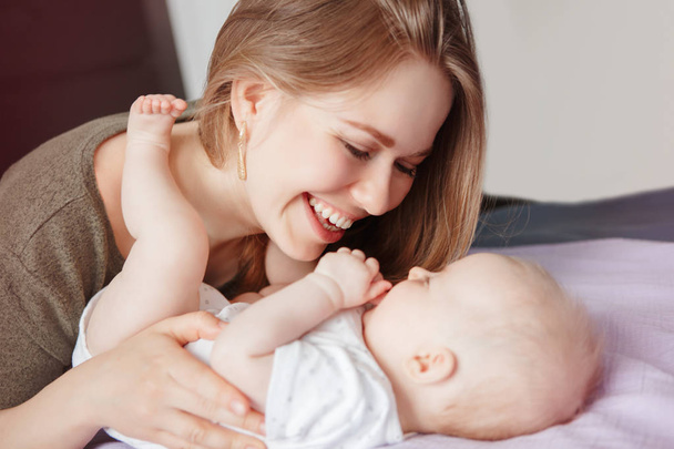 Closeup of young Caucasian woman mother hugging kissing playing with cute newborn baby boy girl child at home. Authentic candid family lifestyle. Happy motherhood and parenting. - Photo, Image