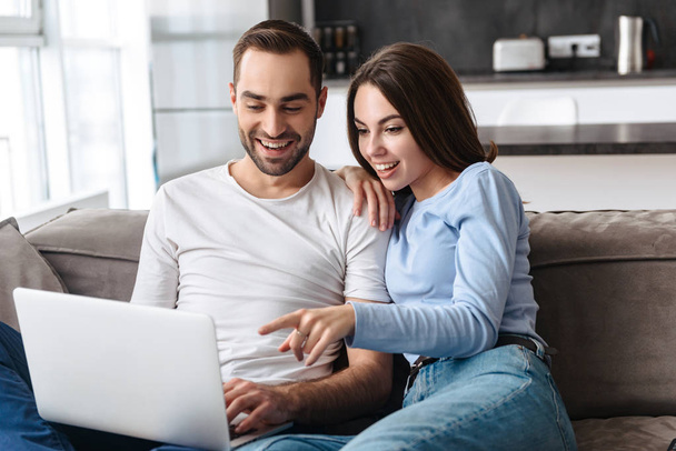 Image of happy couple using laptop together while sitting on sof - 写真・画像