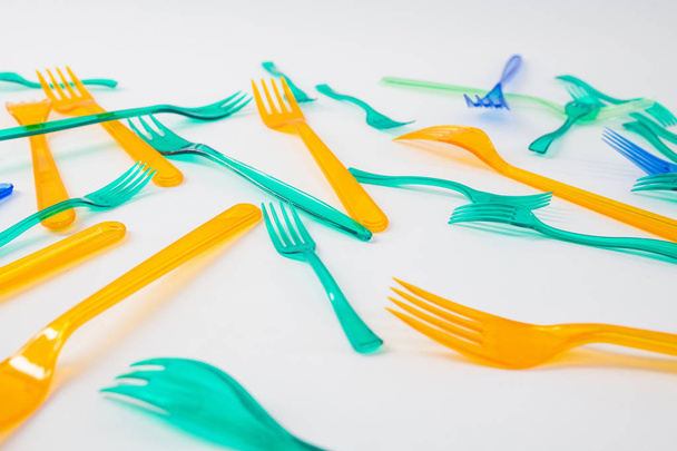 Green and orange transparent forks being placed on white surface - Foto, immagini