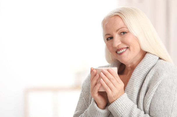 Portrait of beautiful older woman with cup of tea against blurred background. Space for text - 写真・画像