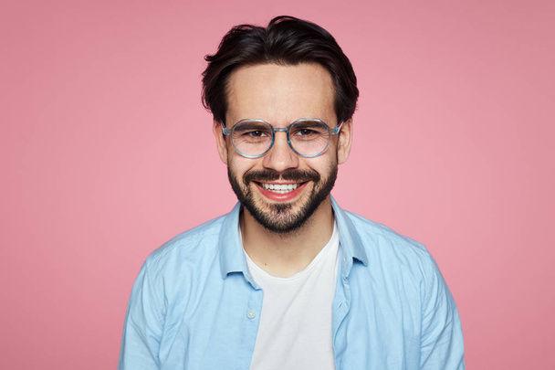 Attraente hipster maschio sorridente alla fotocamera, felice di trovare un lavoro adatto ben pagato, isolato su sfondo rosa
. - Foto, immagini