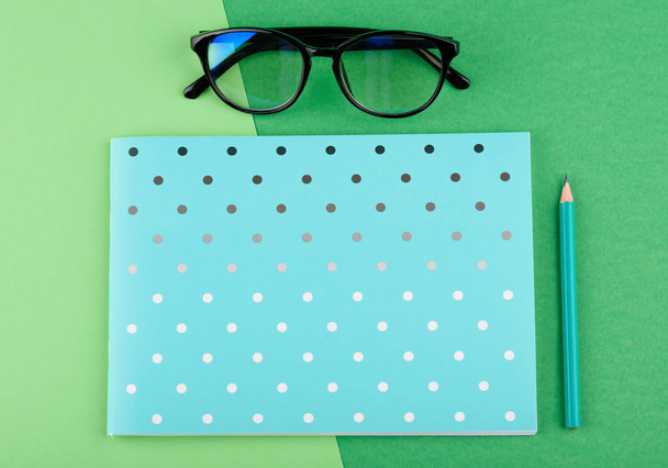Caderno azul com um lápis, óculos, em um fundo verde
 - Foto, Imagem