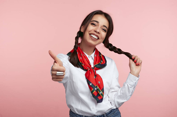 Young attractive girl shows like gesture, satisfied with something, wearing white shirt and scarf, standing over pink background - Fotografie, Obrázek