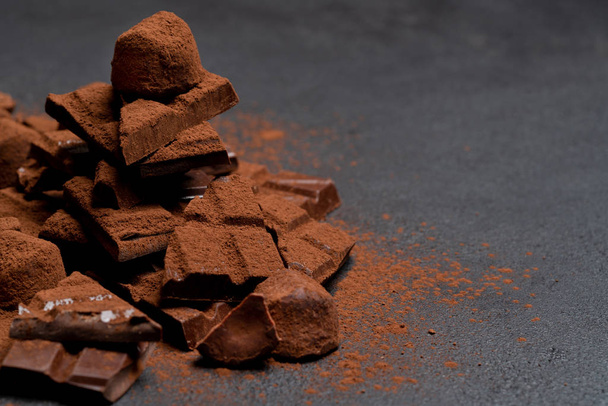 Dark or milk organic chocolate pieces, cocoa powder and truffle candies on dark concrete backgound - 写真・画像