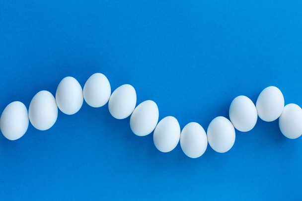 Białe jaja kurze na niebieskim tle pokryte falą. Zdrowa żywność organiczna i koncepcja diety. Temat wielkanocny - Zdjęcie, obraz