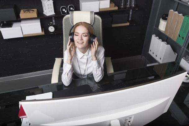 Blonde fille dans une chemise blanche écouter de la musique dans le bureau
 - Photo, image