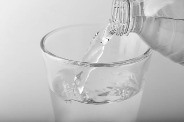Наливаючи воду в склянку на світлому фоні, крупним планом
 - Фото, зображення