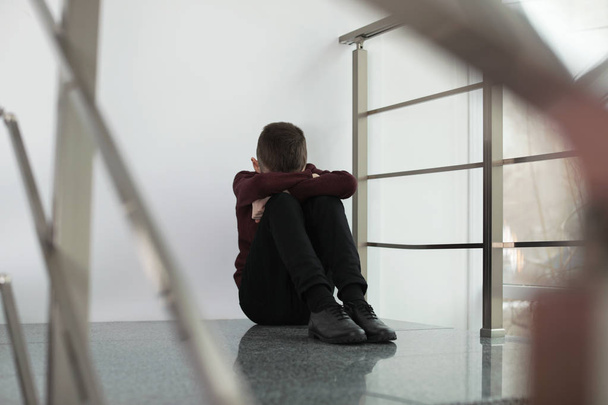 Upset preteen boy sitting on staircase indoors - Valokuva, kuva