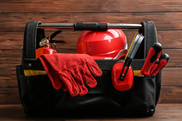 Black bag with construction tools on table against wooden background - Photo, Image