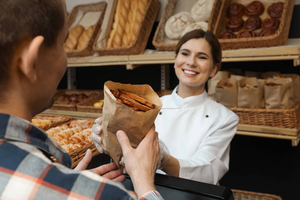 Baker giving customer paper bag with pastry in store - Foto, Bild