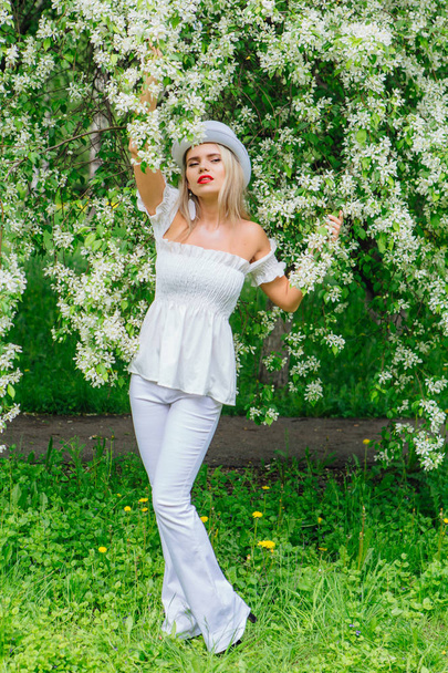 Sexy modern bride in white cylinder hat enjoing blooming apple tree flowers. - Zdjęcie, obraz