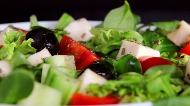 Gezonde voeding. Salade van Groenen en plakjes kaas tomaten en komkommers. Plaat close-up draait op een zwarte achtergrond - Video