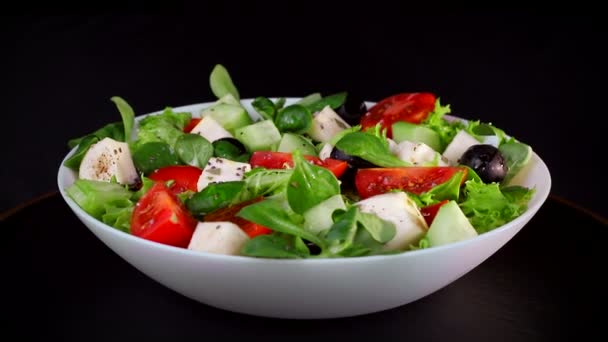 Dieta saludable. La ensalada de la verdura y los trozos del queso los tomates y los pepinos. La placa gira sobre un fondo negro
 - Imágenes, Vídeo